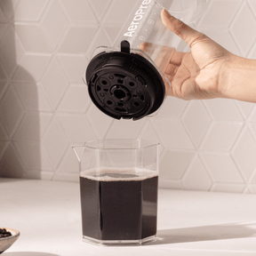 Person using an AeroPress to make coffee on a white countertop.