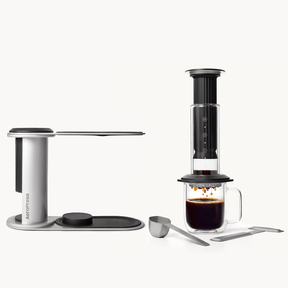 AeroPress Premium Black coffee maker with a glass mug of coffee on a white background #color_black