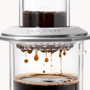 AeroPress Premium coffee maker with coffee being pressed through, showing the brewing process. #color_silver