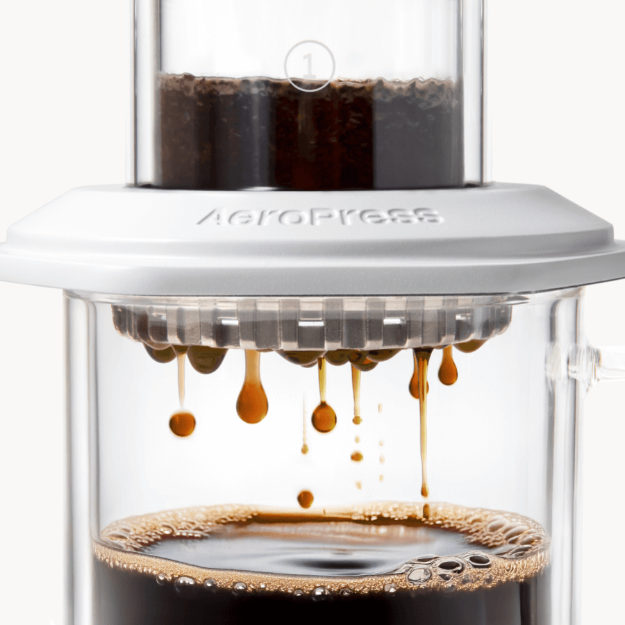 AeroPress Premium coffee maker with coffee being pressed through, showing the brewing process. #color_white
