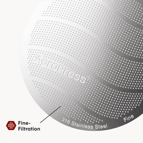 Close-up of an AeroPress coffee maker with 'AeroPress' branding and text indicating 316 stainless steel and fine filtration. #color_blue