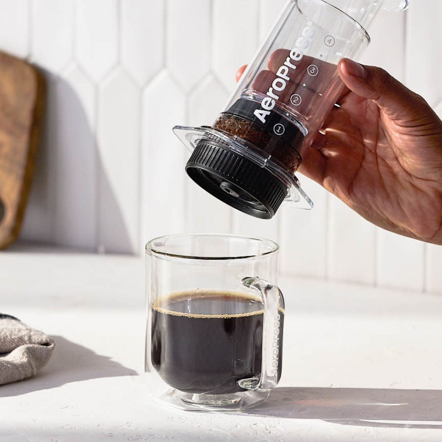 Hand lifting away an AeroPress Clear coffee maker from a clear glass mug full of coffee #color_purple