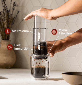 Person using an Aeropress coffee maker with labeled features on a kitchen counter. #color_clear