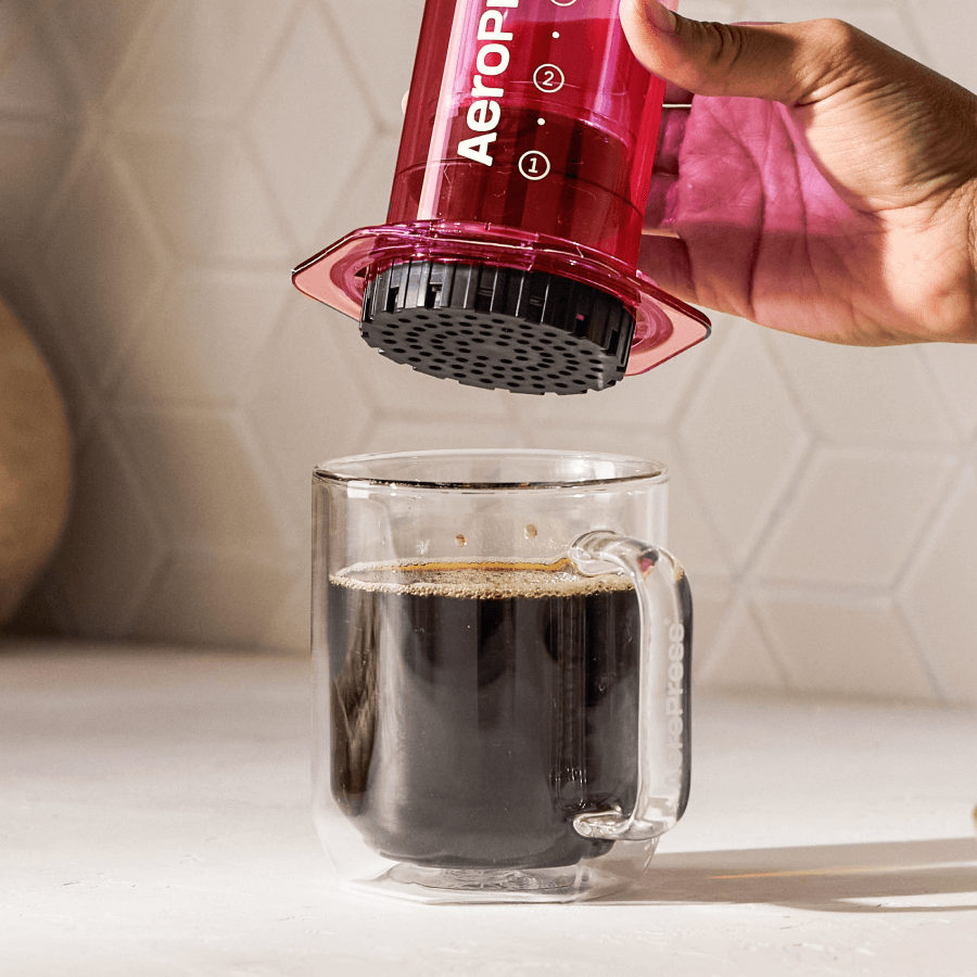 Person using an Aeropress to make coffee in a clear mug. #color_pink