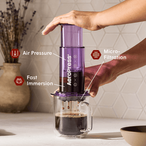 Person using an Aeropress coffee maker with labeled features on a kitchen counter. #color_purple