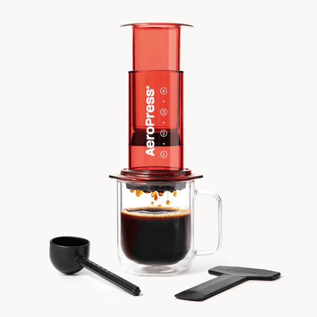AeroPress coffee maker with a glass mug of coffee and scoop on a white background #color_red