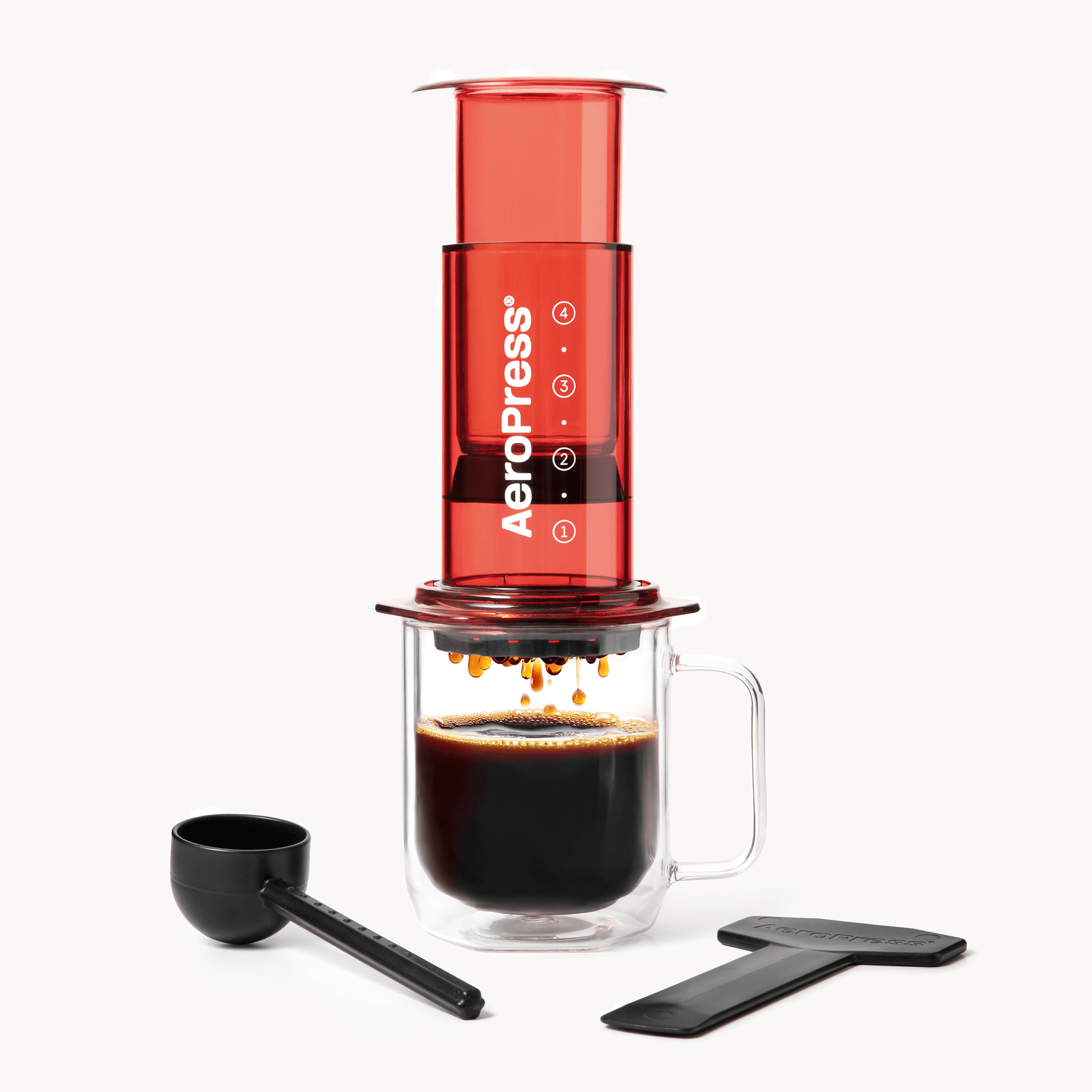 AeroPress coffee maker with a glass mug of coffee and scoop on a white background #color_red