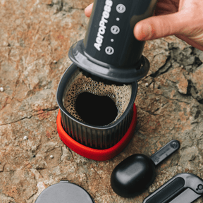 A person using an AeroPress Go Travel coffee maker on a stone surface