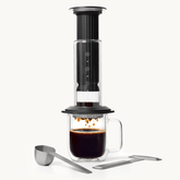 Black AeroPress Premium coffee maker with glass mug on a white background #color_black