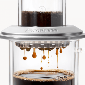 AeroPress Premium coffee maker with coffee being pressed through, showing the brewing process. #color_silver