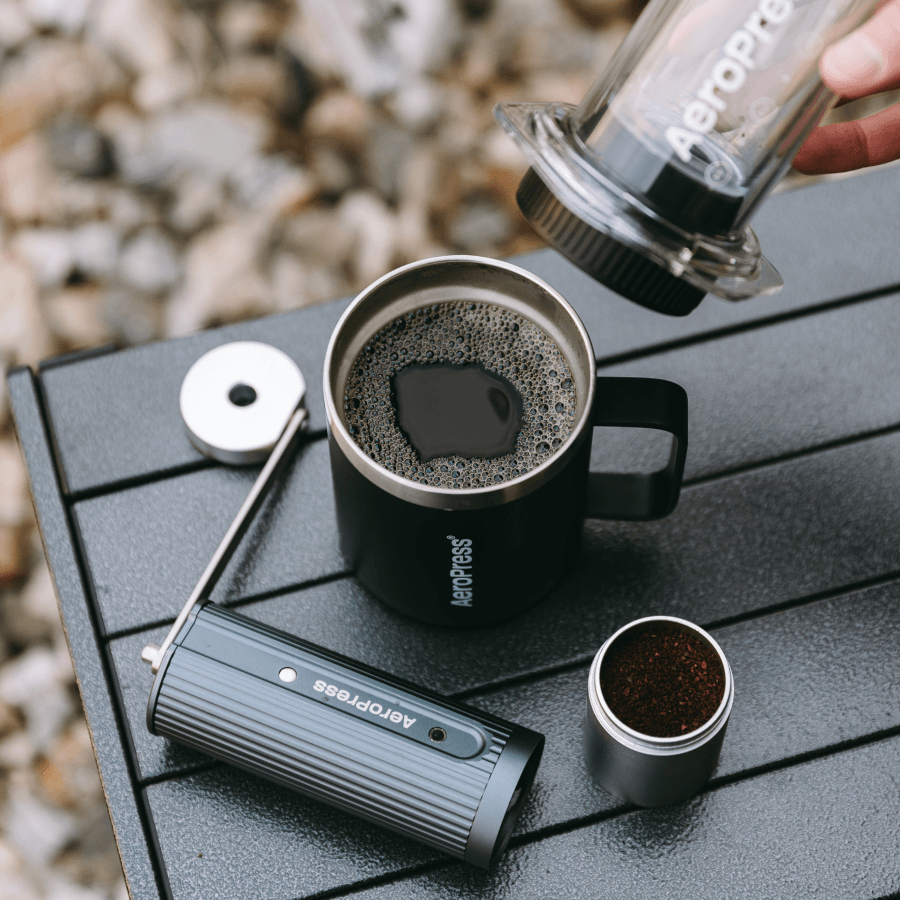 Aeropress coffee maker being used to pour coffee into a black mug on a wooden surface. #color_Purple