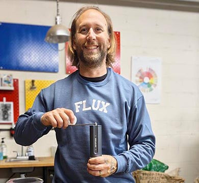 Person holding a manual coffee grinder in a workshop setting.