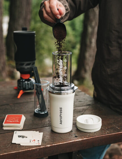 Adding coffee grounds to AeroPress Go Plus travel coffee maker on outdoor table