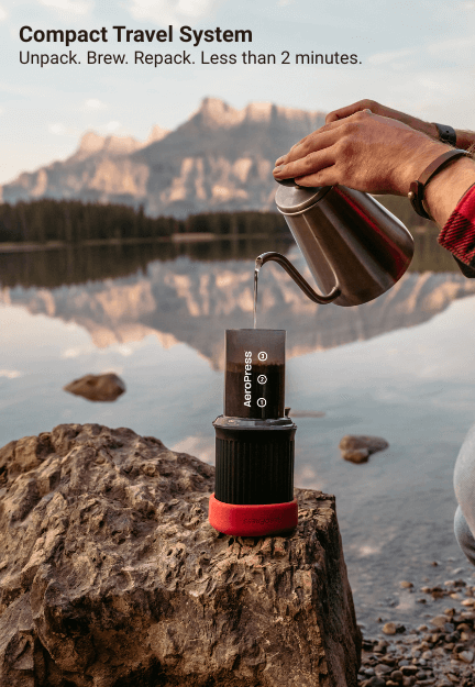 Pouring hot water into AeroPress Go on a rock by a mountain lake